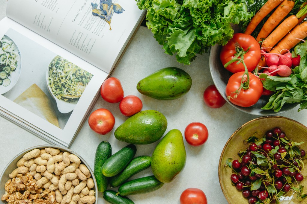 Fresh vegetables, fruit, nuts, and a cookbook arranged for balanced everyday nutrition